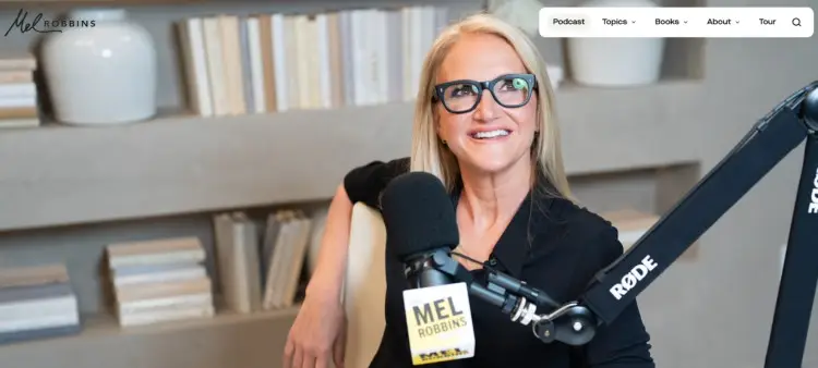 A visually appealing photo of Mel Robbins smiling at her podcast recording setup with a RODE microphone and branded mic flag.