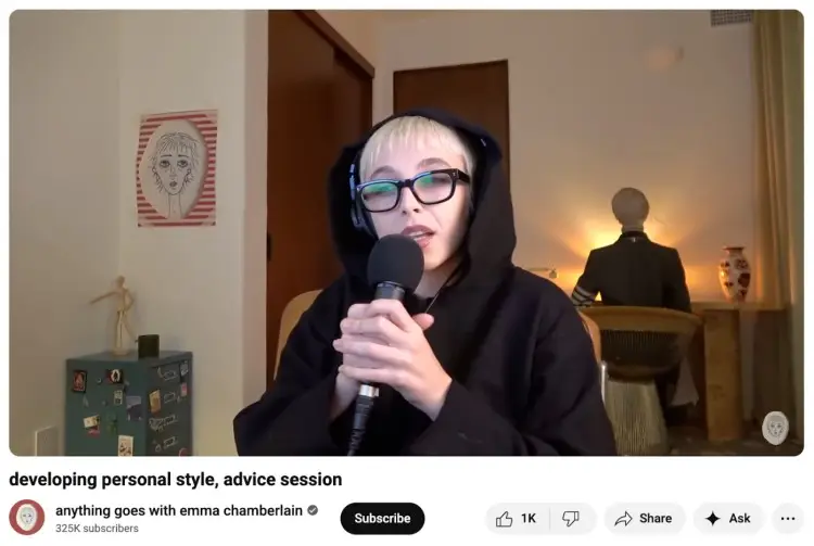 Emma Chamberlain recording her podcast in a dimly lit room with a warm, cozy type of background featuring soft lighting, decor, and a relaxed home-studio vibe.