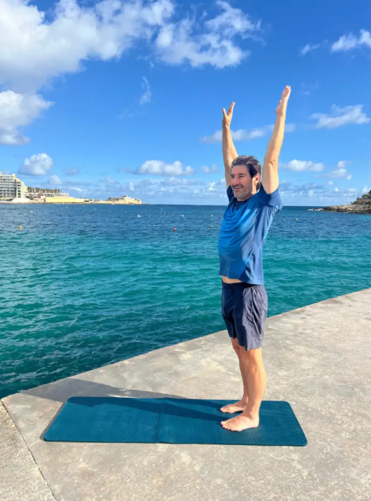 Man standing by the sea with both arms raised overhead to feel more empowered