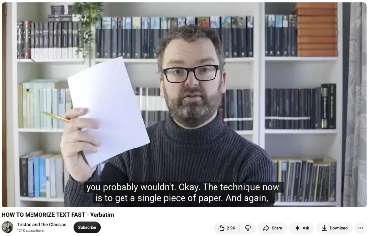 Presenter holding a blank sheet of paper while explaining a technique for memorizing a speech verbatim, with bookshelves in the background.